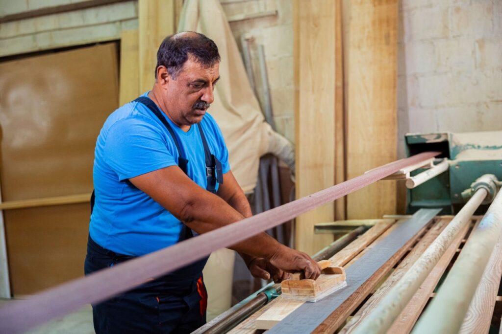 Worker processing long wooden planks on industrial machine inside Eternowoods factory
