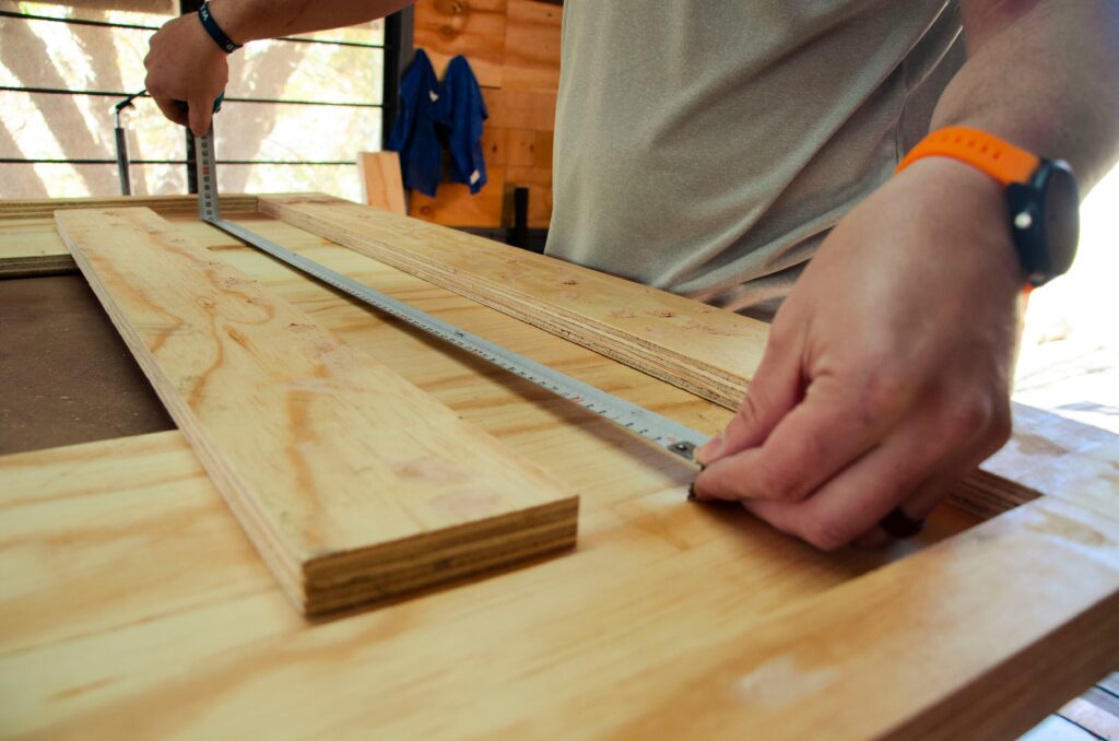 Craftsman measuring plywood sheet on a wooden workbench